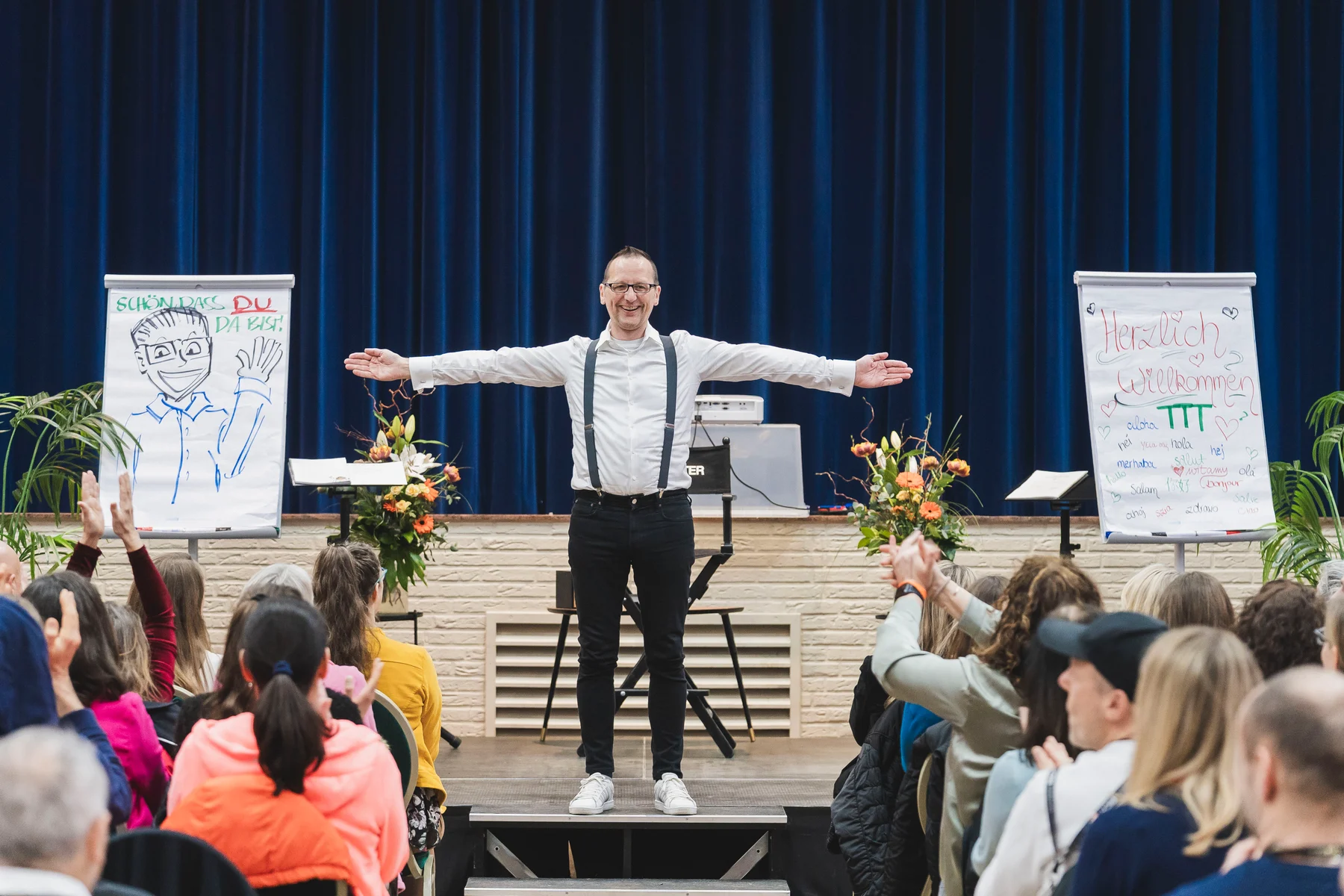 Matthias Istel steht mit offenen Armen vor einem Publikum auf einer Workshopbühne